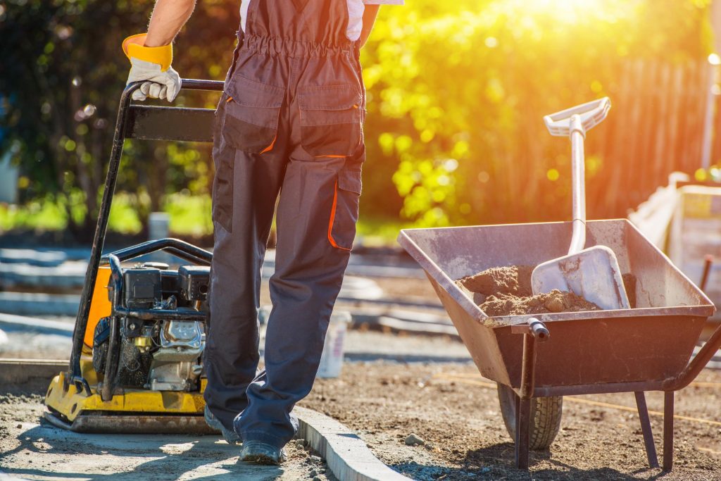man wearing his working clothes using an equipment to flatten the soil