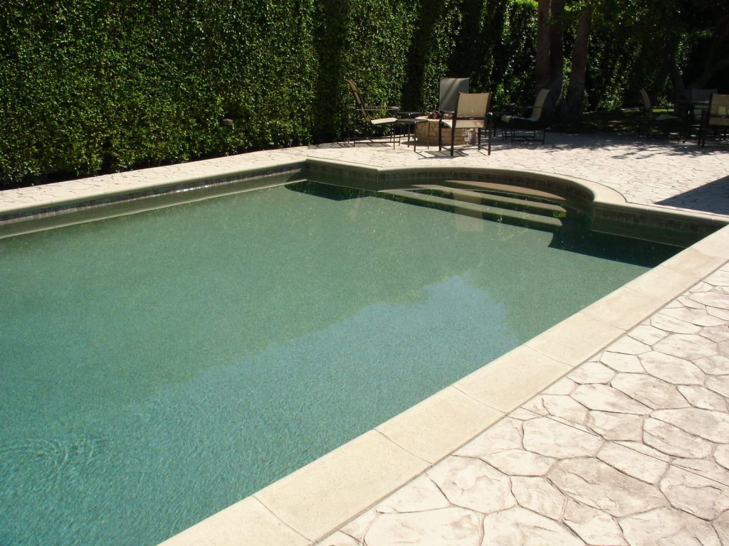 pool filld water with textures floor and surrounded by hedge